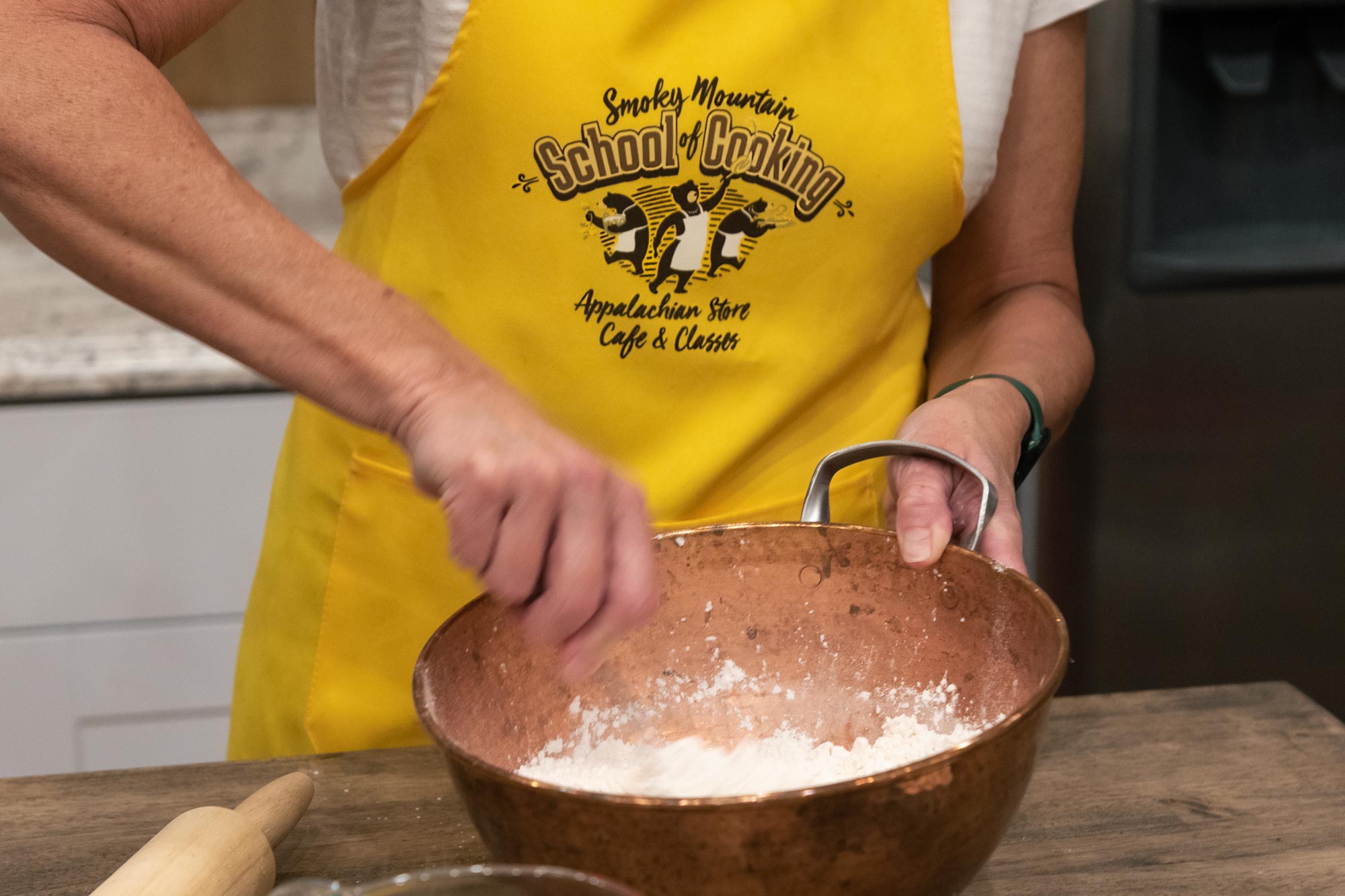 person mixing batter wearing a Smoky Mountain School of Cooking printed apron