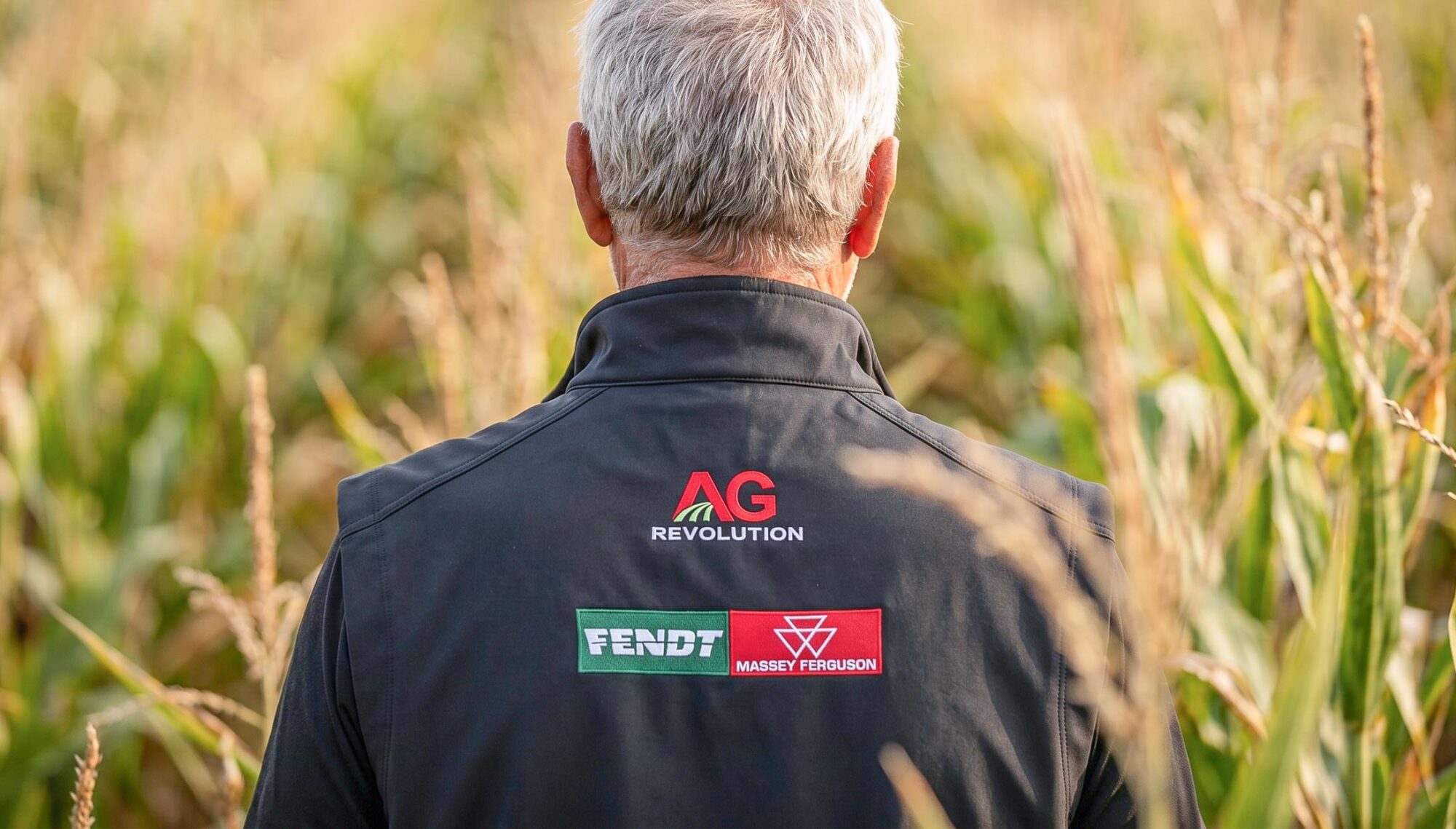 man in corn field wearing embroidered vest with "AG Revolution" logo and "Fendt" logo and "Massey Ferguson" logo