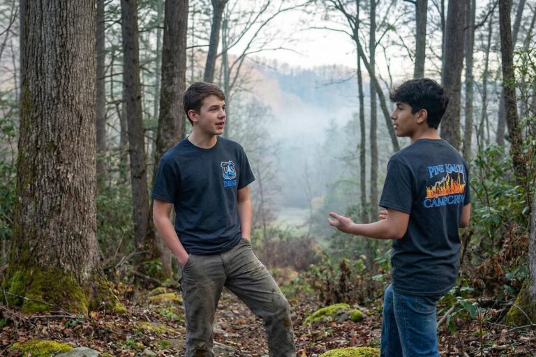 Teenagers in the woods wearing NPACT screen printed t-shirts with "Pine Knot Camp Crew" and flame graphjics